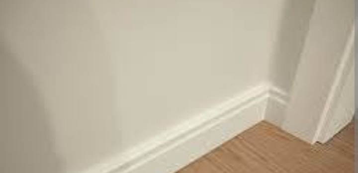 Jasna ściana po malowaniu z białą listwą przypodłogową i fragmentem drewnianej podłogi. Minimalistyczne wykończenie wnętrza, świeżo po remoncie.