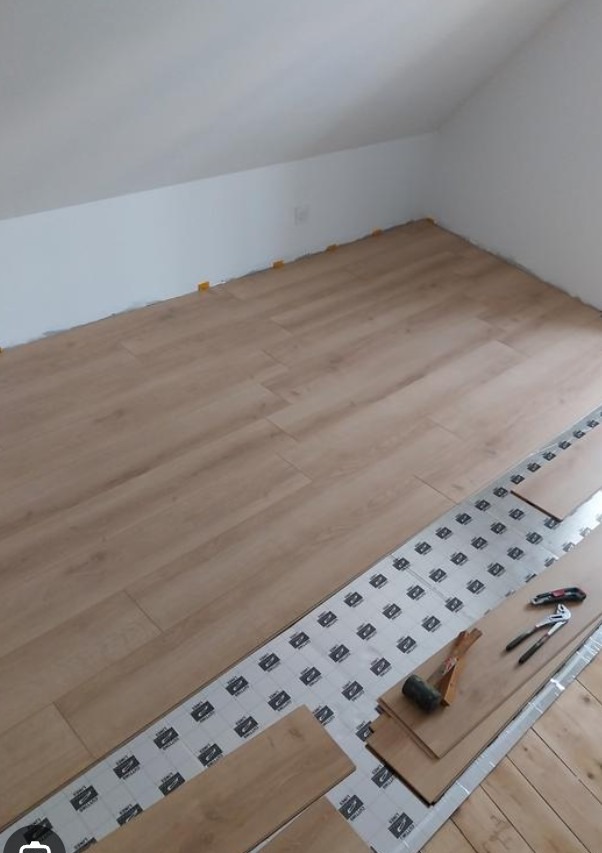 Układanie paneli podłogowych w pokoju na poddaszu w Nowej Rudzie. Widoczne narzędzia i podkład pod panele. Jasne panele ułożone częściowo.