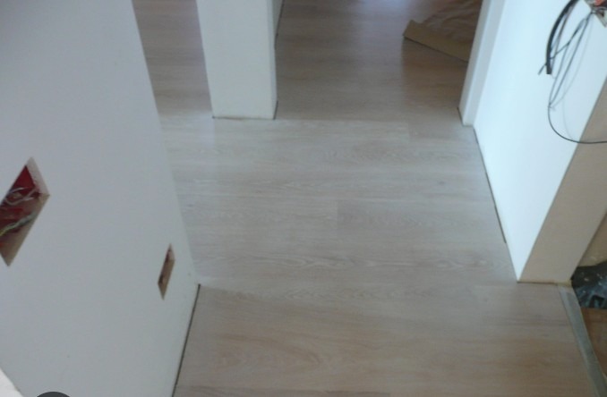 Jasne panele podłogowe ułożone w nowym mieszkaniu, widoczne fragmenty ścian z instalacją elektryczną. Minimalistyczne wykończenie wnętrza.