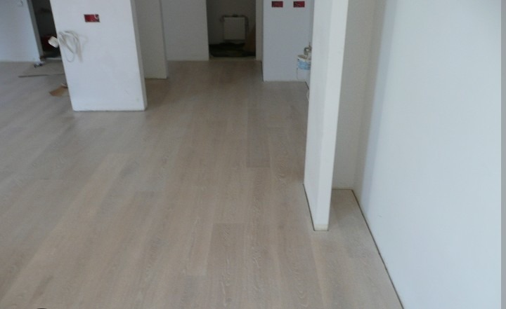 Jasne panele podłogowe ułożone w nowym mieszkaniu, widok z perspektywy podłogi, białe ściany i przygotowane otwory na instalacje elektryczne w tle.