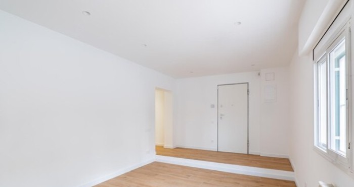 Jasne, puste wnętrze po remoncie: świeżo pomalowane ściany, panele podłogowe, białe drzwi i okno z roletą. Minimalistyczny design, czystość i porządek.