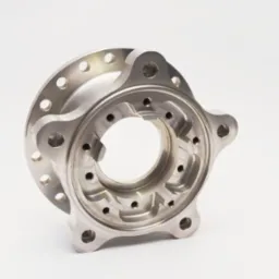 Precyzyjnie wykonany, metalowy element z licznymi otworami i zagłębieniami, obrobiony na jasny, matowy kolor, ustawiony pod kątem na białym tle, ukazujący skomplikowaną geometrię wewnętrzną.