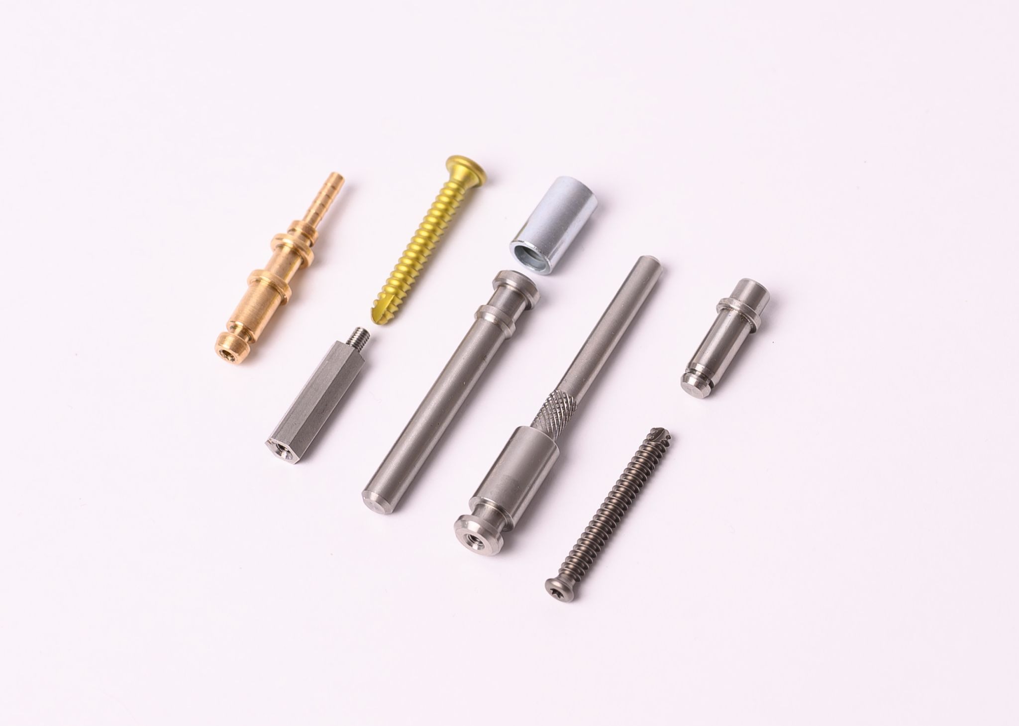 Precyzyjnie wykonane metalowe elementy, w tym mosiężny łącznik z karbowanymi końcówkami, śruba z żółtego metalu i stalowe trzpienie, ułożone na białym tle, prezentujące różnorodność obróbki CNC.