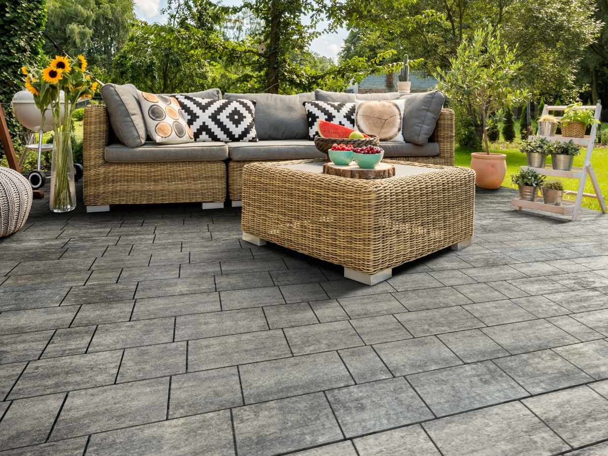 Szara nawierzchnia z prostokątnych elementów ułożona na tarasie, z rattanowym zestawem wypoczynkowym i dekoracjami ogrodowymi w tle.