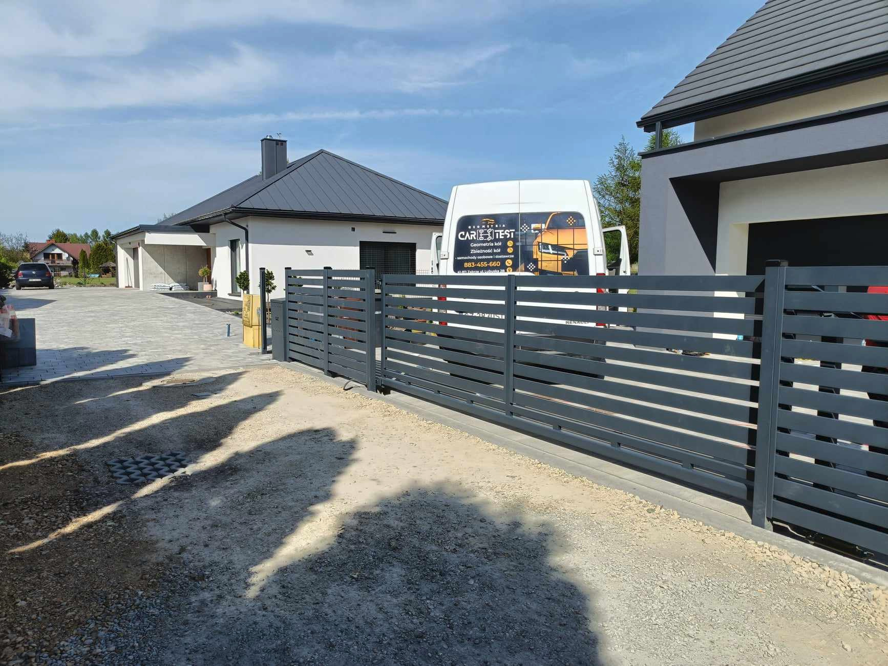 Nowoczesne, poziome, szare przęsła ogrodzeniowe na posesji z domem i zaparkowanym busem firmy świadczącej usługi.