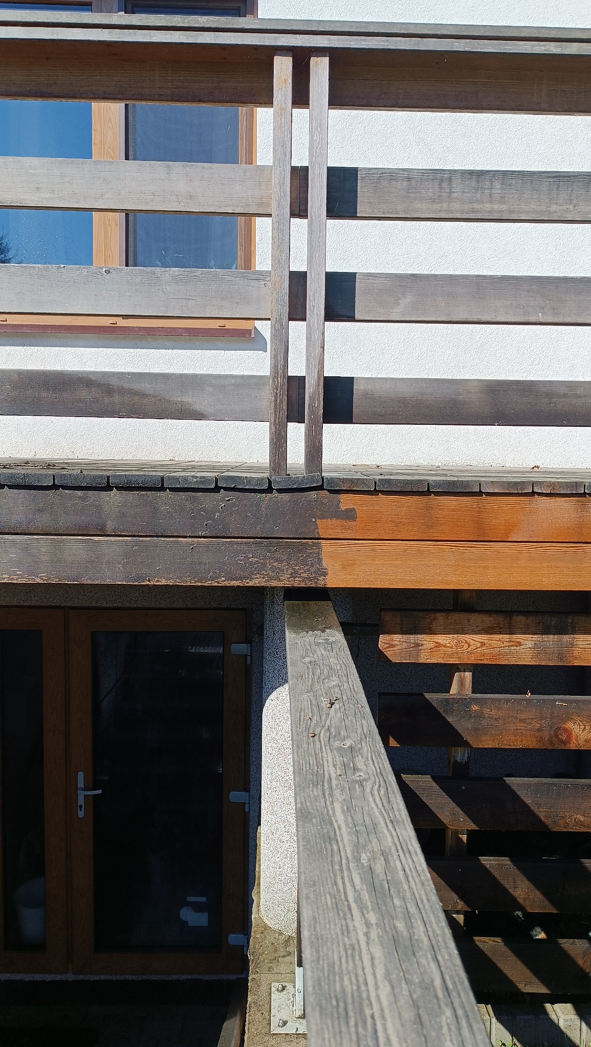 Fragment drewnianego tarasu przed i po czyszczeniu, widoczna różnica w kolorze drewna, z lewej strony powierzchnia nieczyszczona, z prawej odświeżona, jaśniejsza.