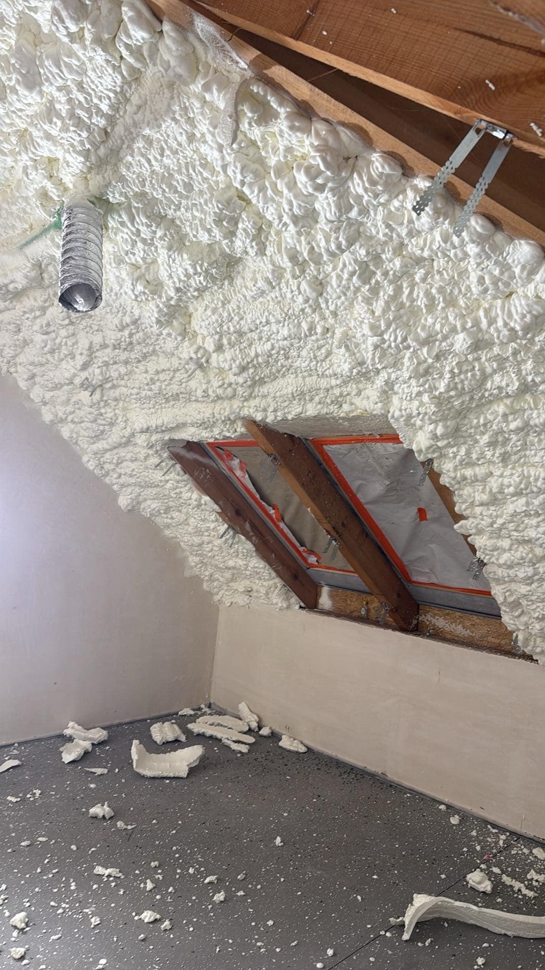Poddasze ocieplone pianką PUR z widocznymi elementami drewnianej konstrukcji dachu i resztkami pianki na podłodze.