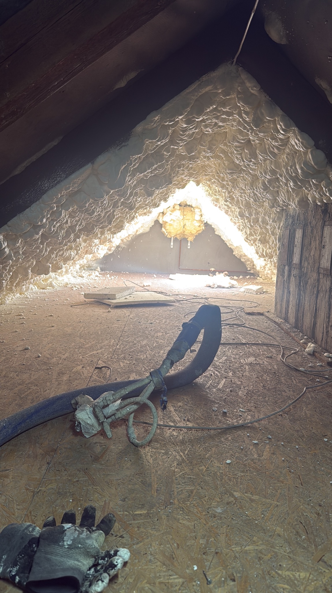 Poddasze po ociepleniu pianką PUR, widoczny sprzęt do natrysku i rękawice robocze. Izolacja pokrywa skośne ściany i sufit, tworząc jednolitą warstwę.