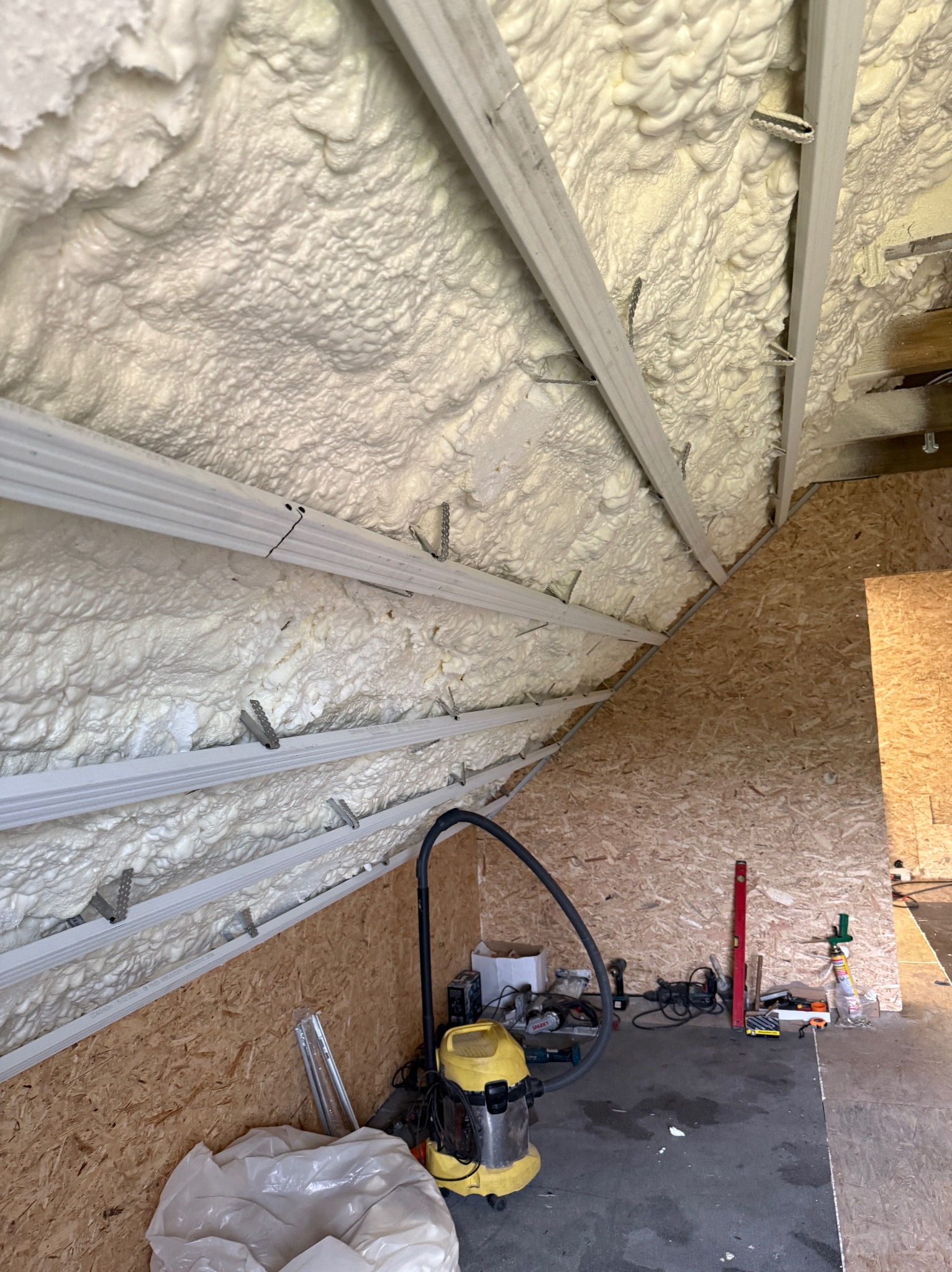 Ocieplony poddasze pianką PUR, widoczne krokwie i narzędzia pracy. Gotowa izolacja termiczna wewnątrz budynku.