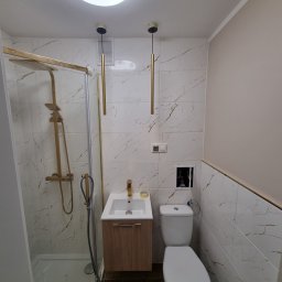 AUTORYZOWANY SERWIS DARIUSZ KASZOWSKI - Nowoczesna łazienka z kabiną prysznicową ze złotymi elementami, umywalką z szafką w odcieniach drewna, toaletą i marmurowymi płytkami ściennymi z brązowymi żyłkami.