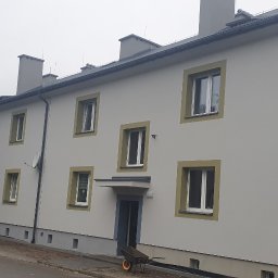 LIS BARTŁOMIEJ ZAKŁAD REMONTOWO-BUDOWLANY - Odnowiona elewacja dwupiętrowego budynku z szarymi oknami i numerem 'Pilotów 4' na rogu. Widoczny fragment samochodu i pracownik przy wejściu.