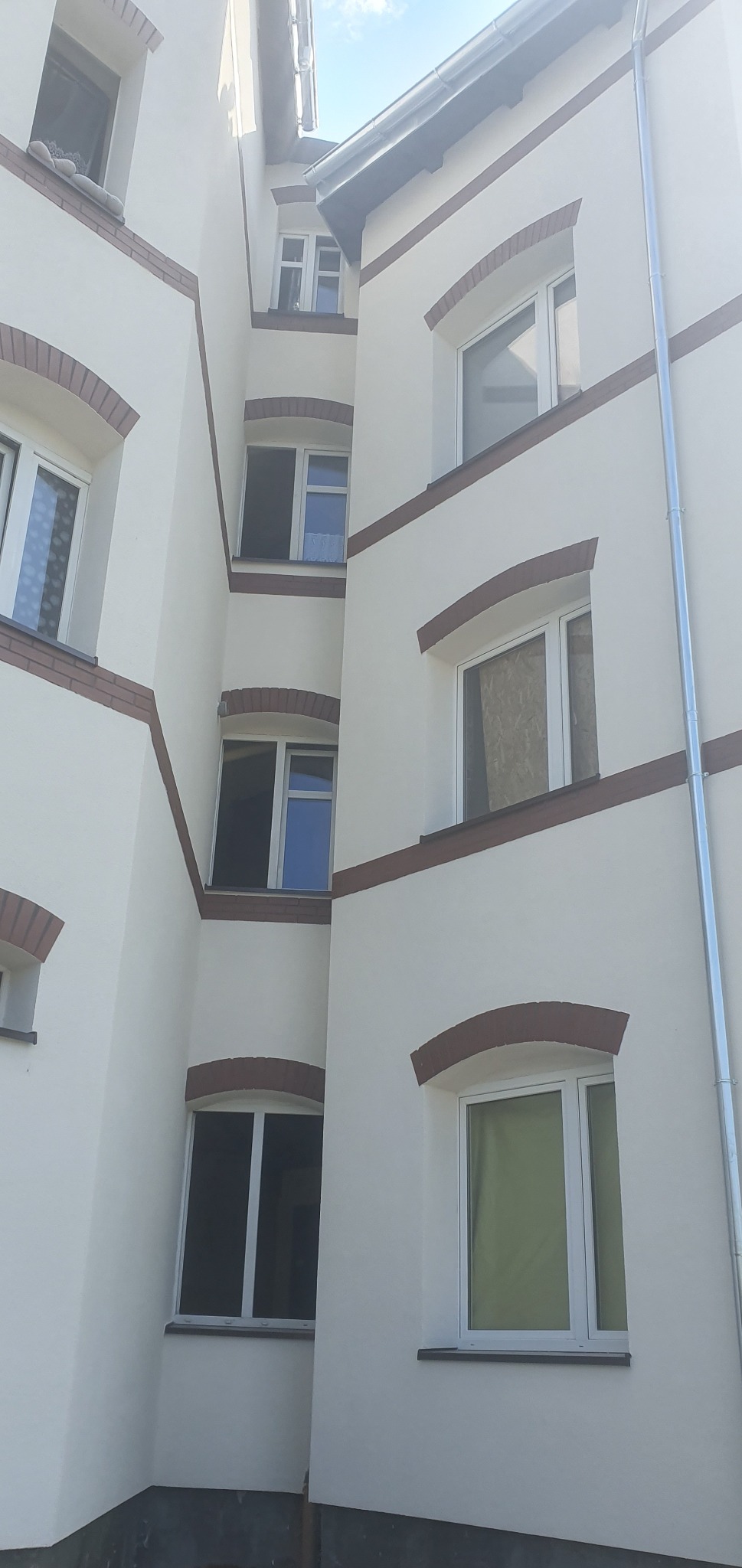 Odnowiona elewacja budynku z białymi ścianami i ceglanymi detalami wokół okien, widok z dołu, ukazujący geometrię budynku i detale wykończenia.