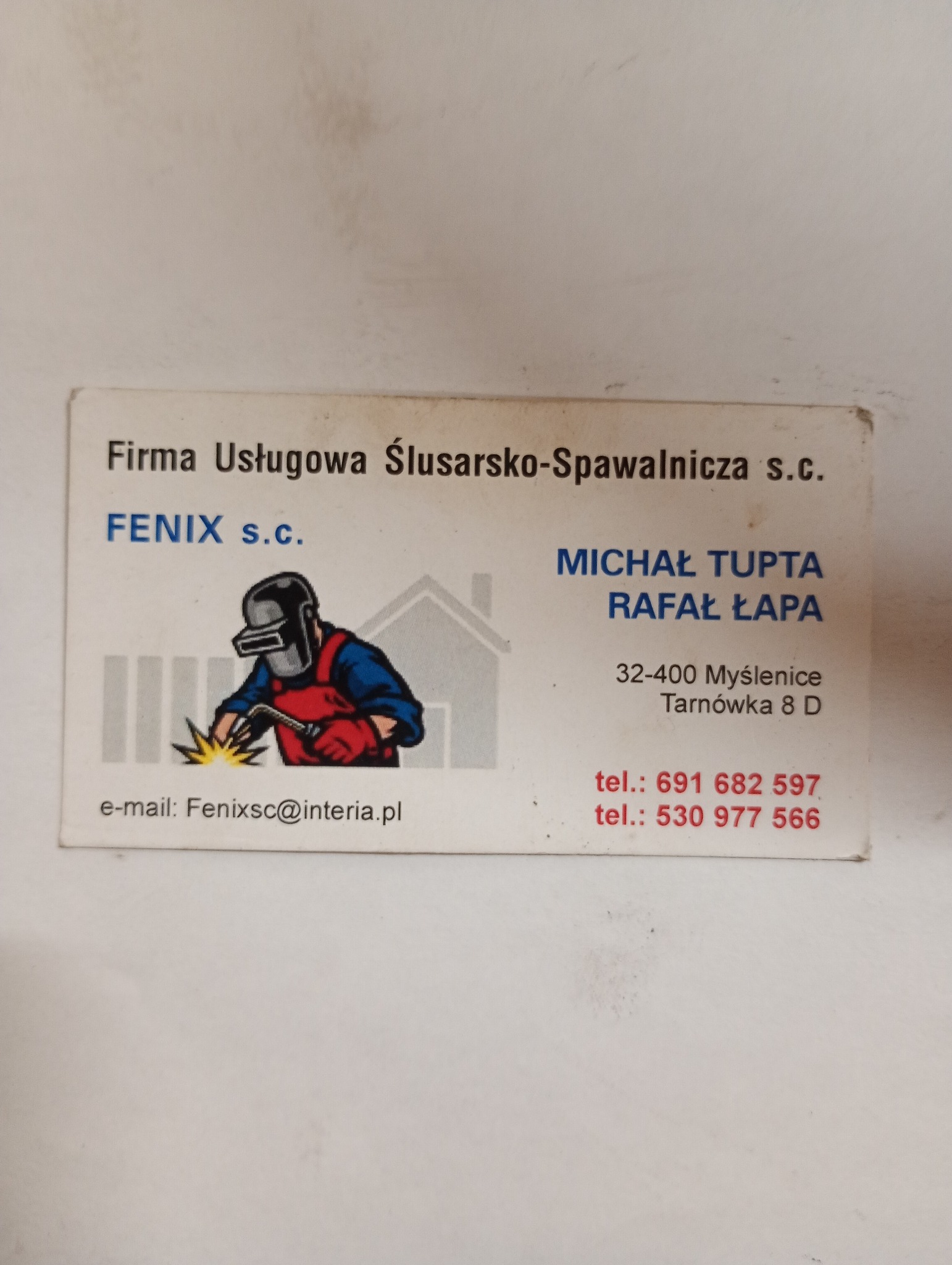 Zdjęcie wizytówki firmy Usługowej Ślusarsko-Spawalniczej FENIX s.c. z ilustracją osoby w masce ochronnej podczas pracy z iskrzącym narzędziem.