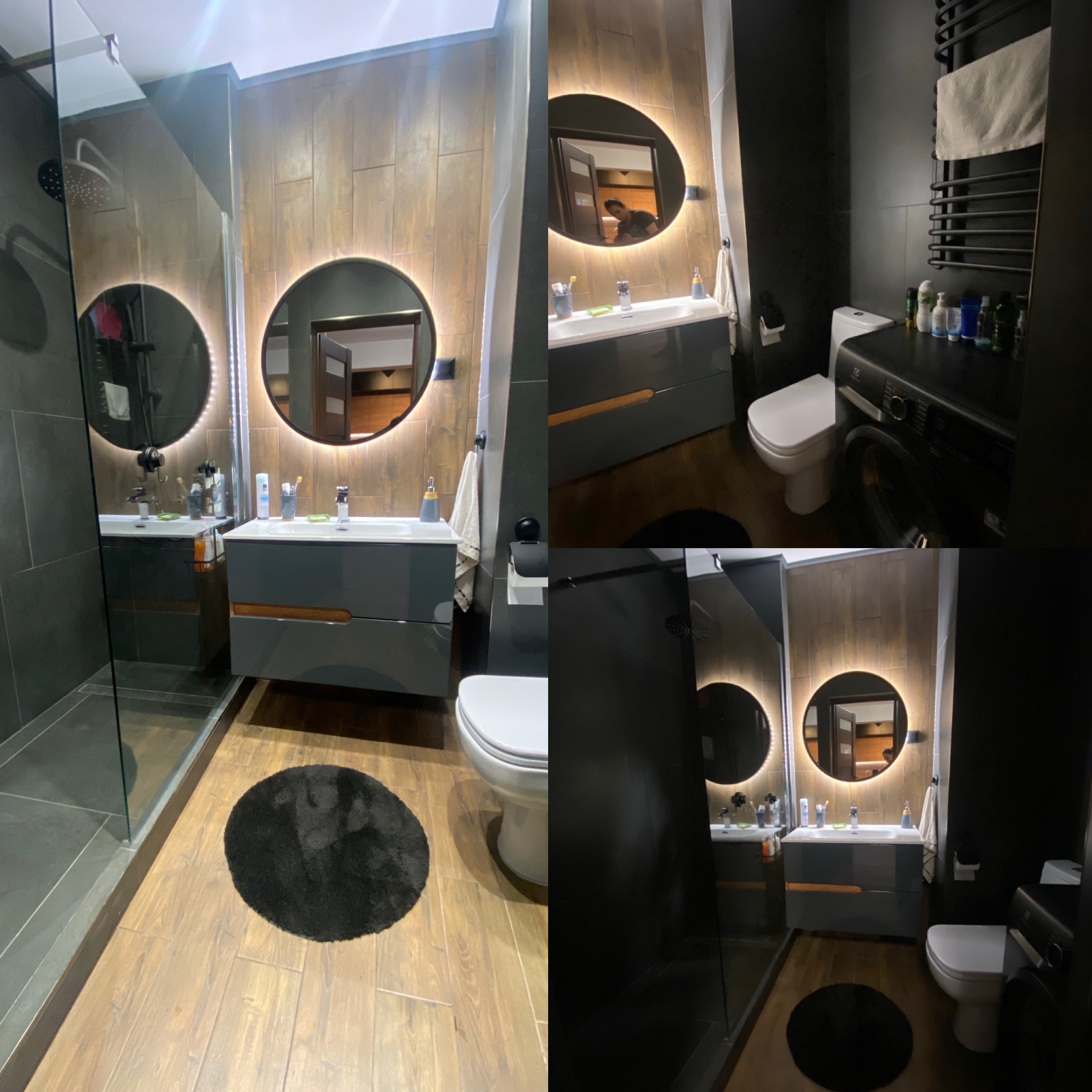 Nowoczesna łazienka z kabiną prysznicową typu walk-in, okrągłym lustrem z podświetleniem LED, szarą szafką pod umywalką z drewnianymi akcentami i czarną ścianą z grzejnikiem drabinkowym.