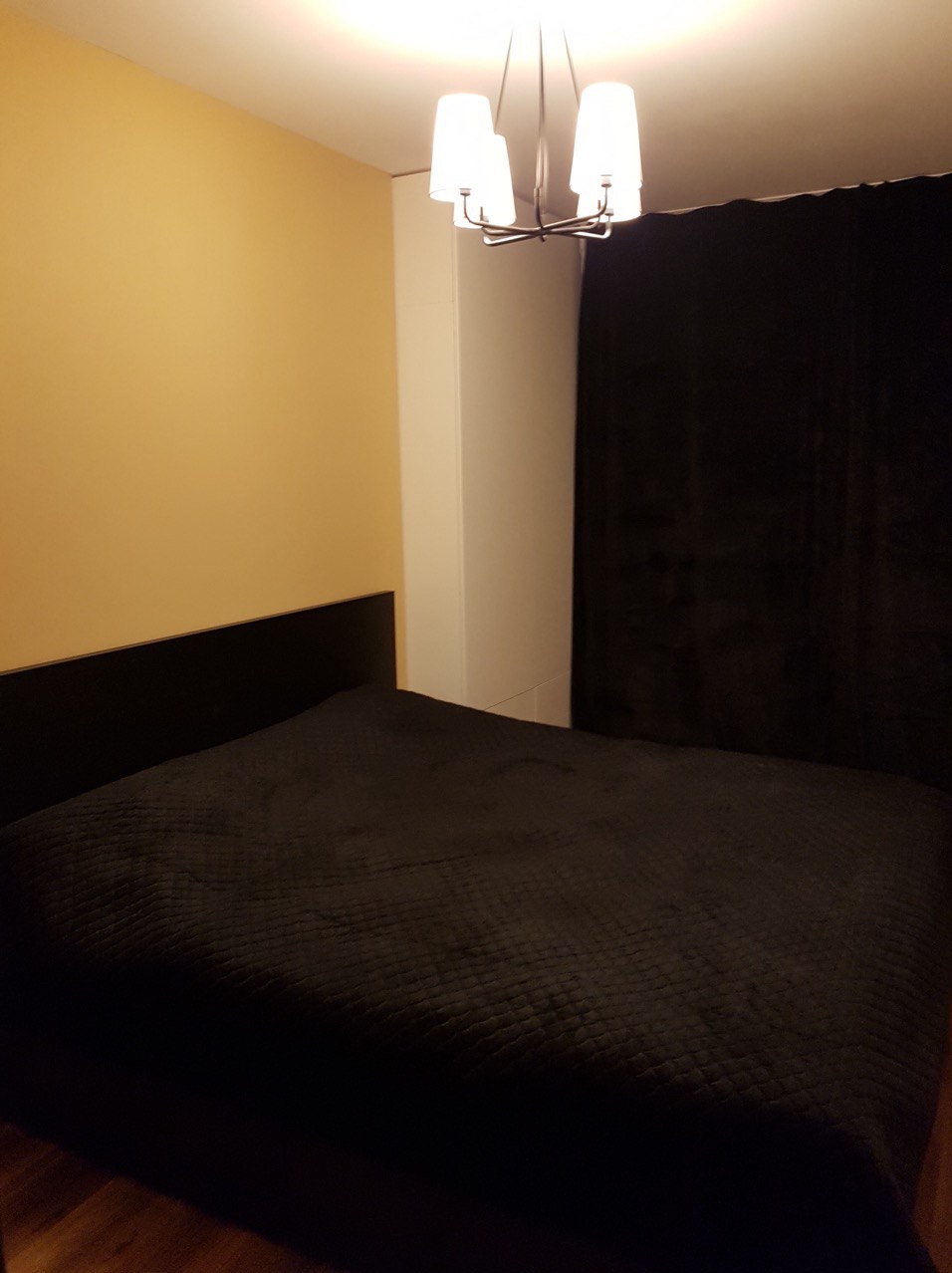 Sypialnia z czarnym łóżkiem, beżową ścianą i nowoczesną lampą sufitową z białymi kloszami.