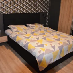 Sypialnia z łóżkiem kontynentalnym, geometryczna tapeta w odcieniach szarości, czerni i złota, drewniana podłoga, szafka nocna z lampką i budzikiem.