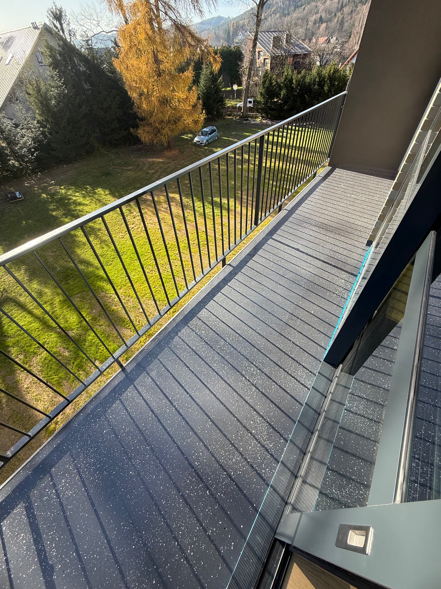 Szary balkon z żywiczną posadzką w kropki, czarne metalowe barierki, widok na zieleń i zabudowę. Nowoczesne wykończenie balkonu z dbałością o detale.