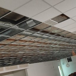 MAR-BUD Mateusz Potyński - Montaż sufitu podwieszanego kasetonowego z widoczną konstrukcją i instalacją wentylacyjną. Pracownik na podnośniku koszowym w tle.