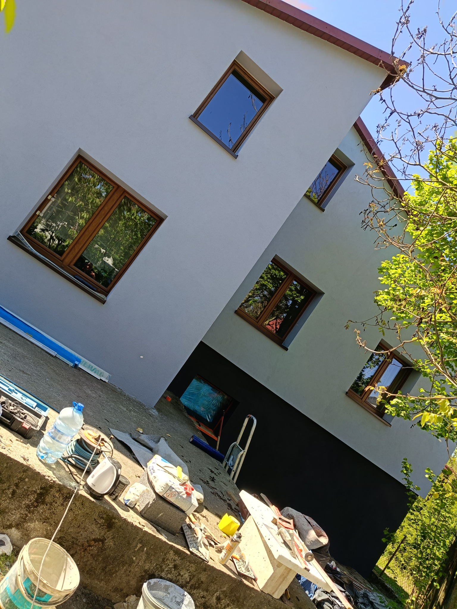 Elewacja budynku po remoncie z nowymi oknami, widok z dołu. Na pierwszym planie narzędzia i materiały budowlane. Ujęcie z perspektywy żabiej.