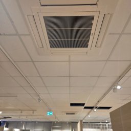 Andrzej Zmurek Stork Went - Kasetonowa klimatyzacja sufitowa Mitsubishi Electric w jasnym wnętrzu sklepu, widok z dołu. Widoczne kratki wentylacyjne i oświetlenie sufitowe.