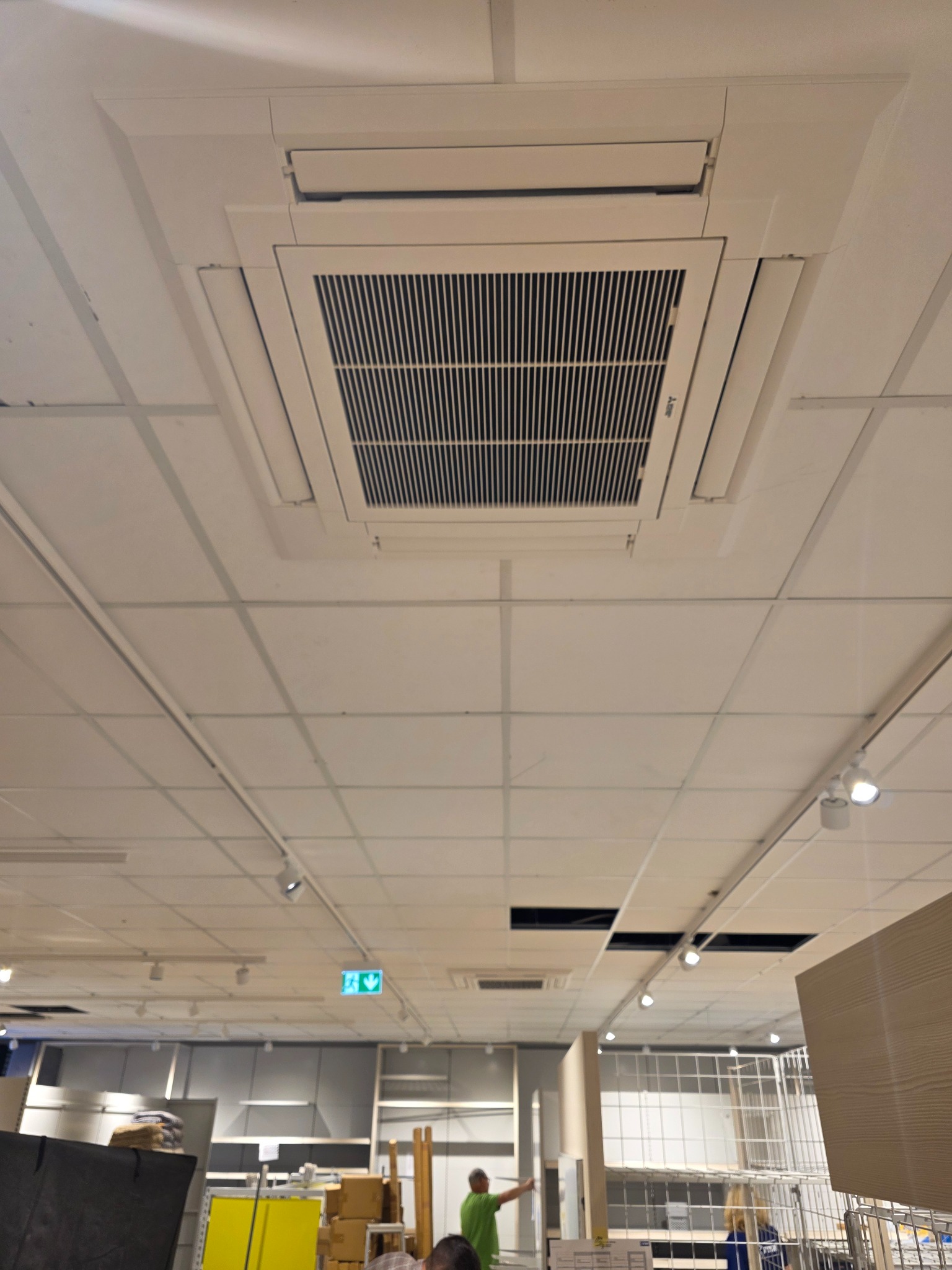 Kasetonowa klimatyzacja sufitowa Mitsubishi Electric w jasnym wnętrzu sklepu, widok z dołu. Widoczne kratki wentylacyjne i oświetlenie sufitowe.
