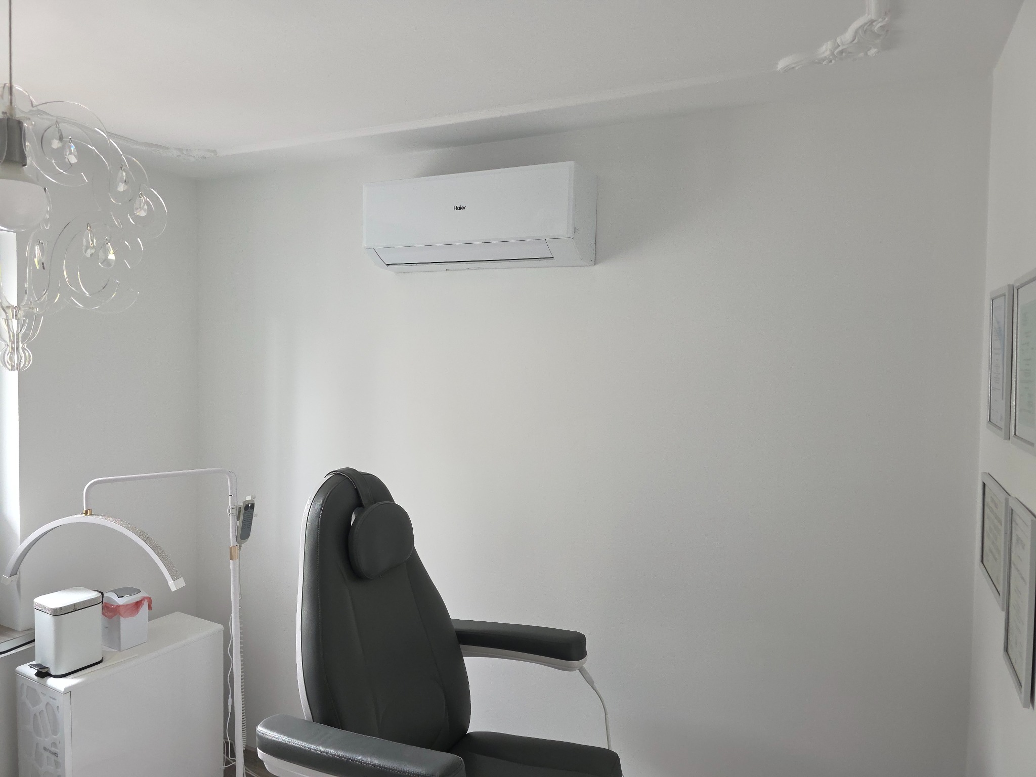 Biały klimatyzator Haier na ścianie w gabinecie kosmetycznym, obok lampa LED i fotel. Minimalistyczne wnętrze, jasne światło.