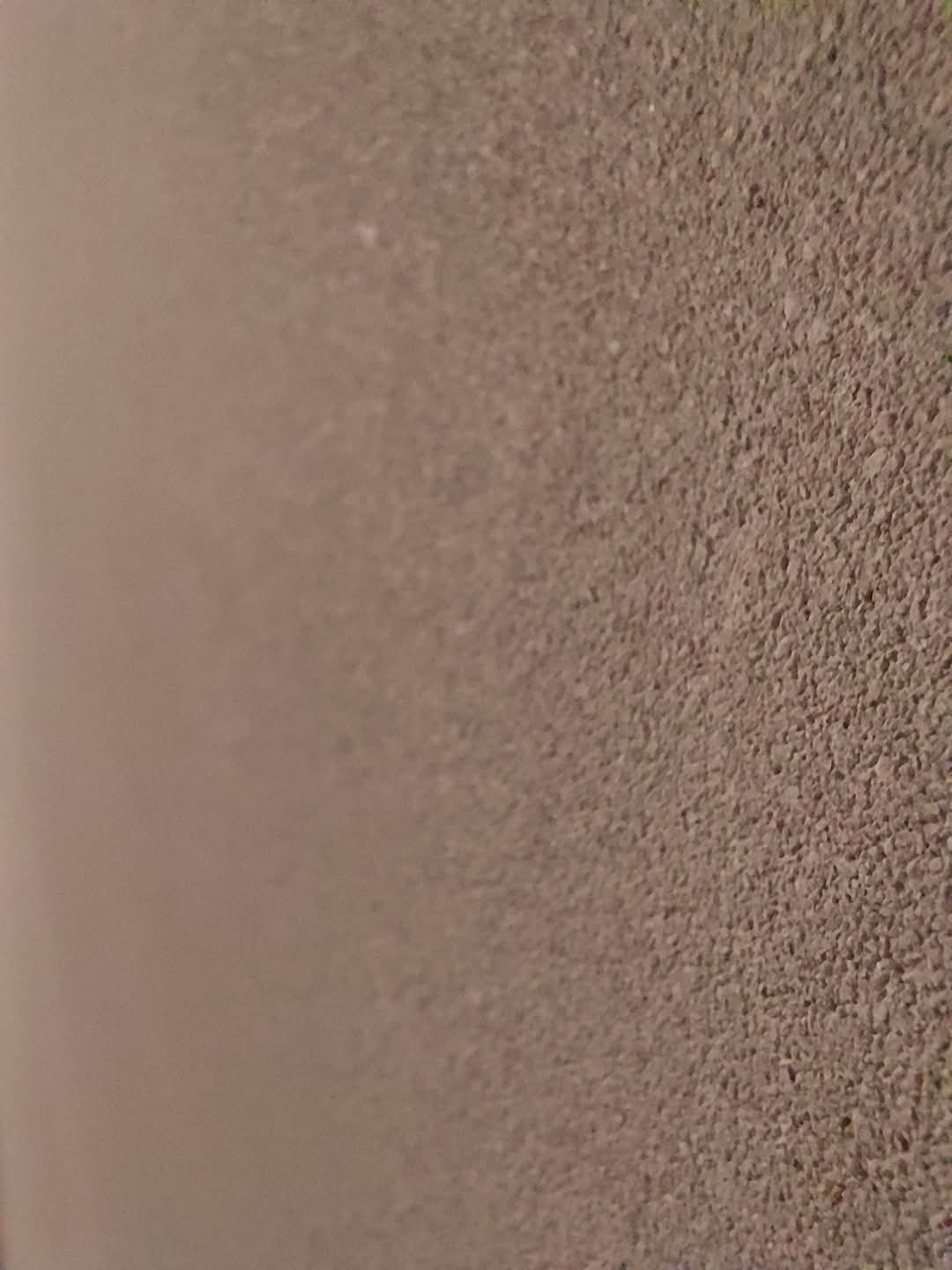 Delikatna, beżowa faktura ściany z bliska, ukazująca równomierne, drobne ziarno tynku. Oświetlenie boczne podkreśla strukturę.