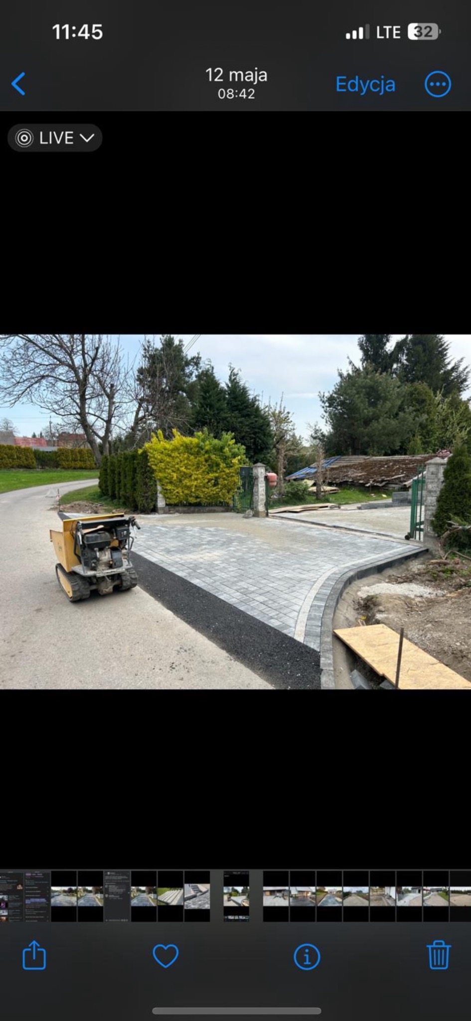 Ukończony podjazd z kostki brukowej w odcieniach szarości, z obrzeżami i przygotowanym podłożem. Widoczny mały wywrotka. Tło: zieleń, drzewa.