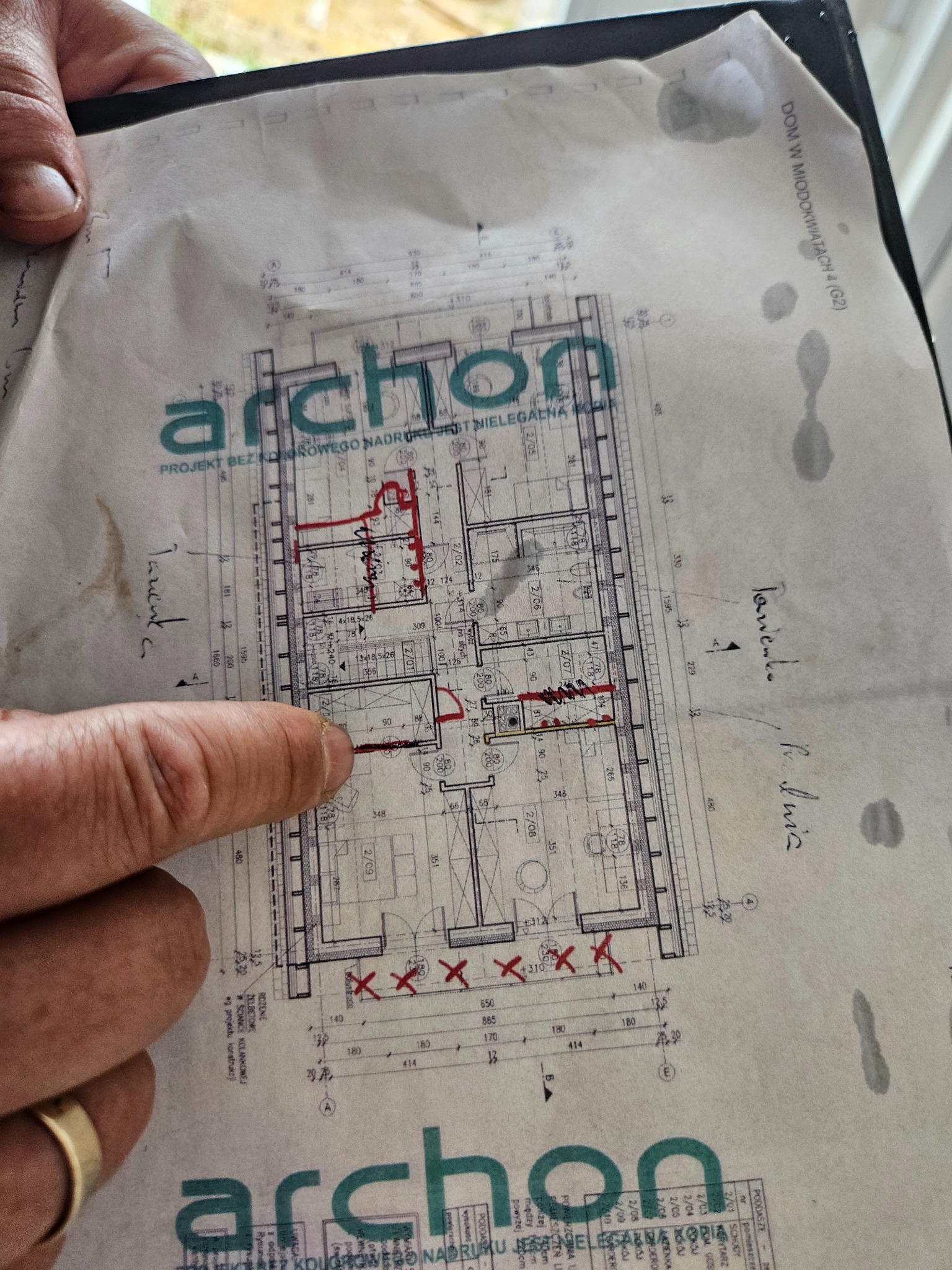 Plan architektoniczny z naniesionymi zmianami instalacji, trzymany w ręce. Widoczne oznaczenia i wymiary pomieszczeń. Projekt archon.