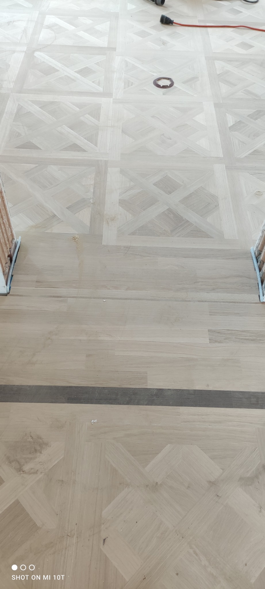 Parkiet ułożony we wzór kwadratów z krzyżami, z widocznymi śladami pyłu i narzędzi, sugerujący etap prac wykończeniowych.