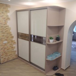 Craftys Mykhailo Tysiachnyi - Beżowa szafa wnękowa z przesuwnymi drzwiami, zdobiona motywem greckim, z półkami na dekoracje, wkomponowana w wystrój wnętrza z elementami cegły.