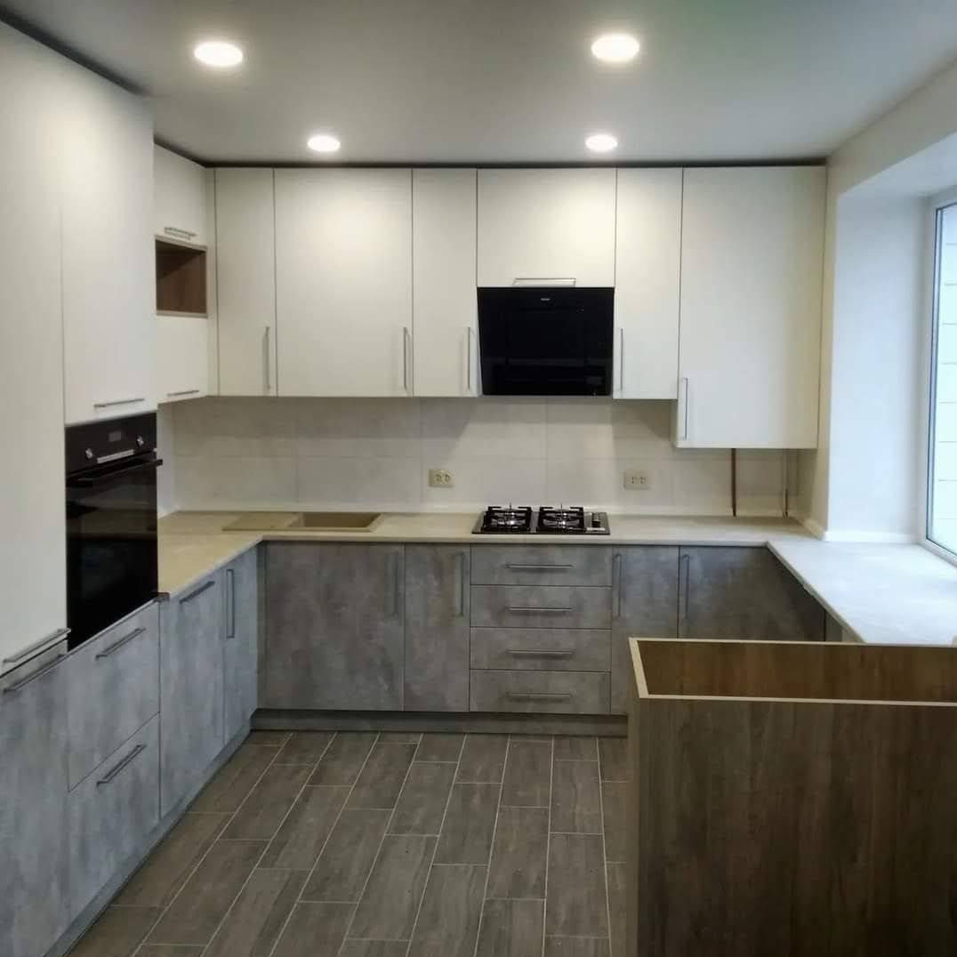 Nowoczesna kuchnia z szarymi i białymi szafkami, płyta gazowa na blacie, okno z parapetem. Minimalistyczny design i funkcjonalne rozwiązanie.