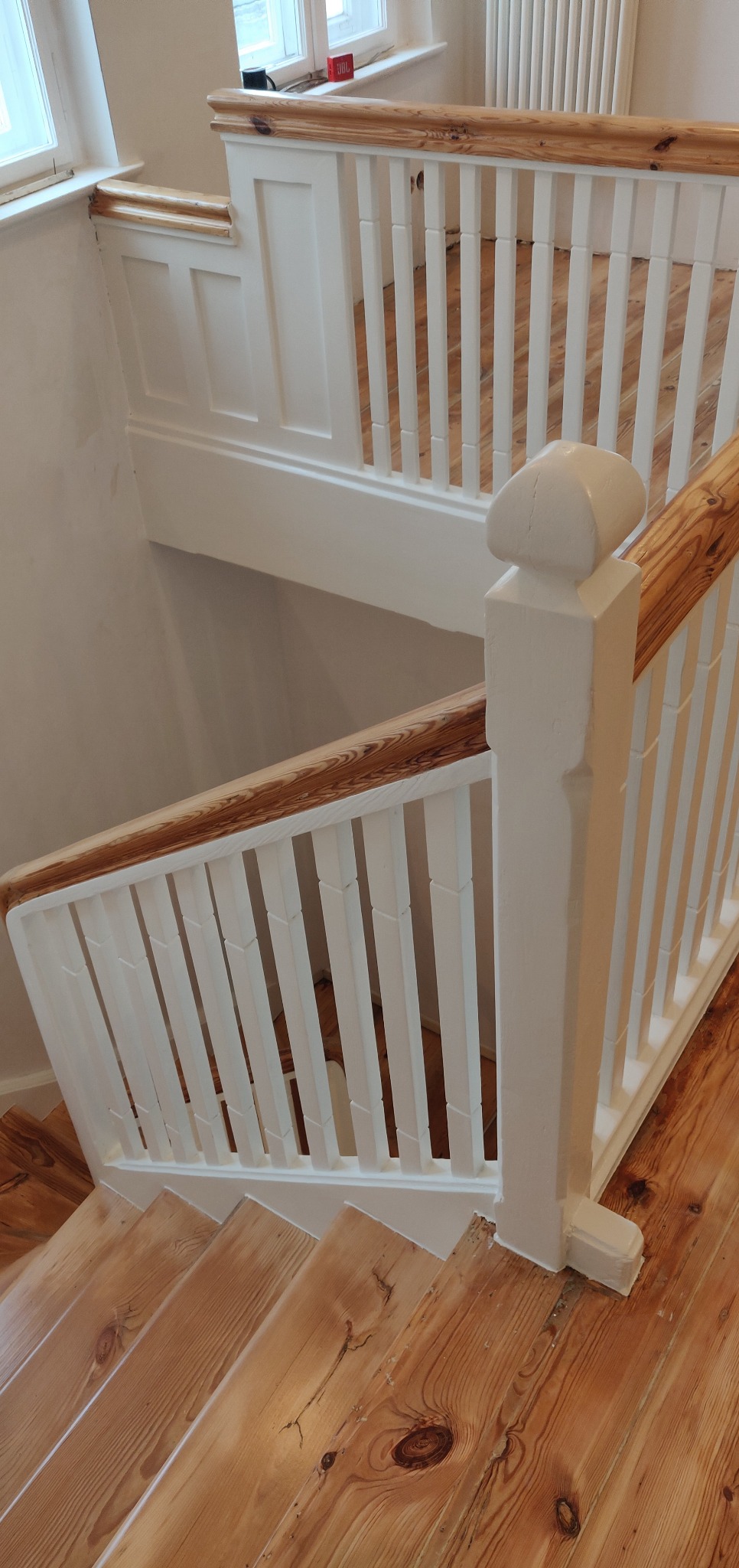Drewniane schody z pomalowanymi na biało balustradami i poręczą z widocznym usłojeniem drewna, po renowacji.