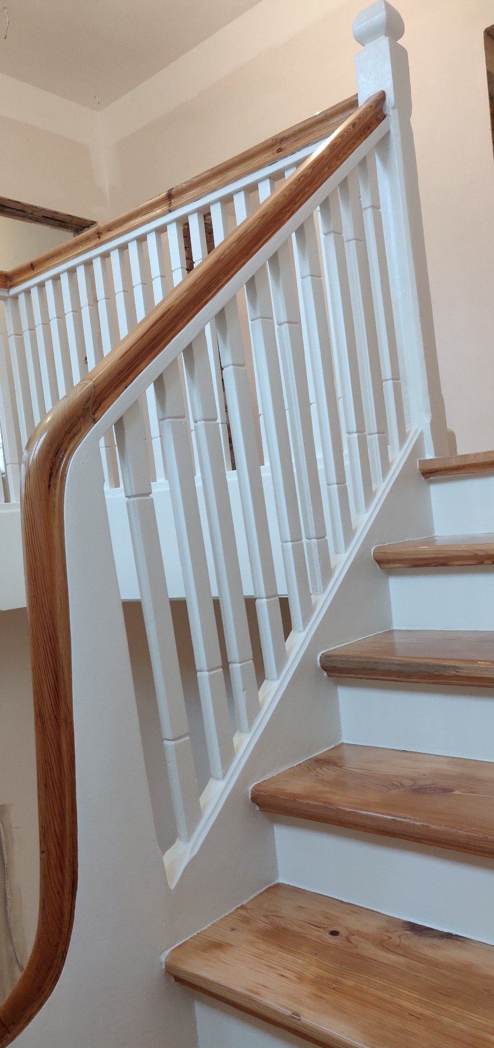 Odnowione drewniane schody z pomalowanymi na biało balustradami, widoczne słoje drewna i detale wykończenia.