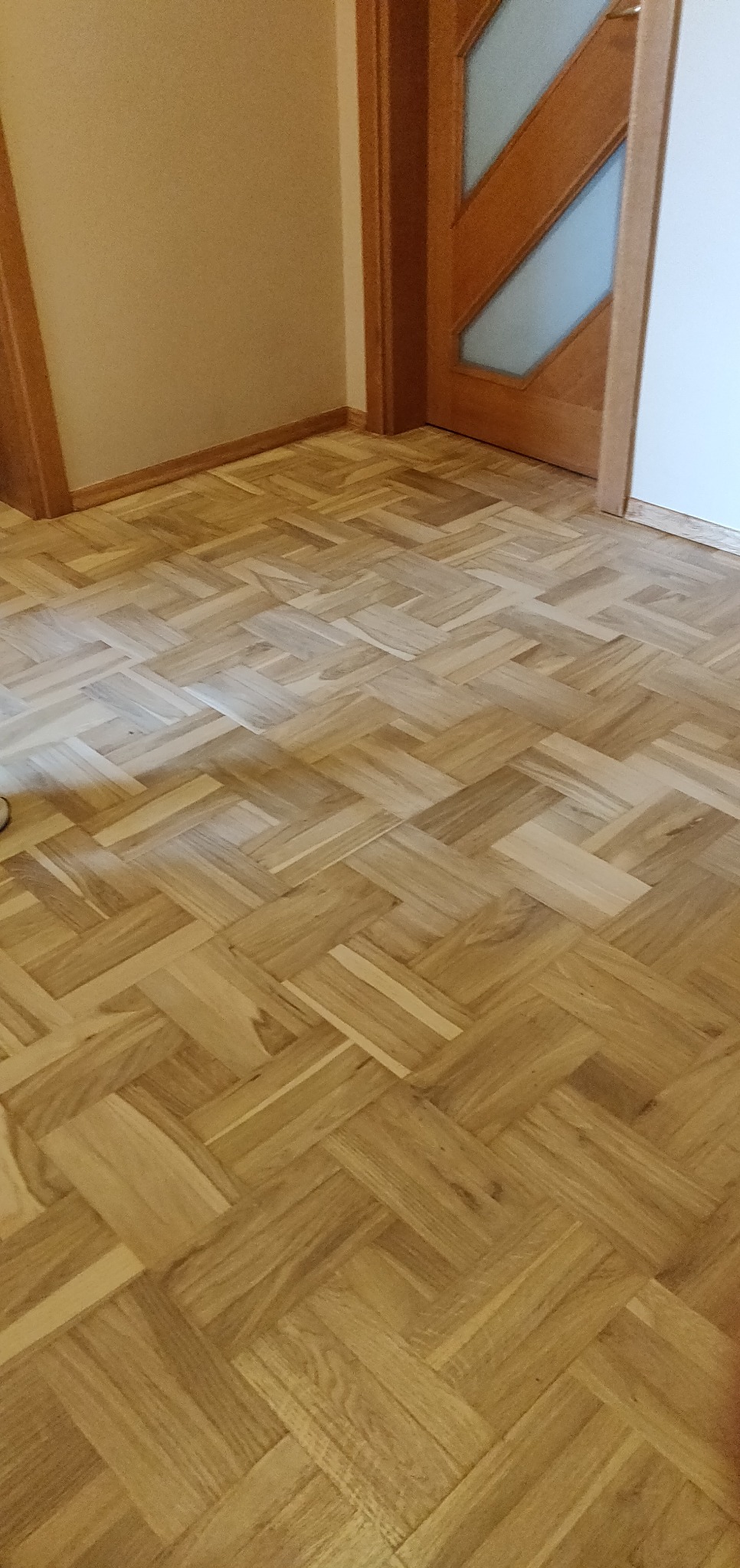 Parkiet ułożony w jodełkę po renowacji, widoczny fragment drzwi z szybą w tle