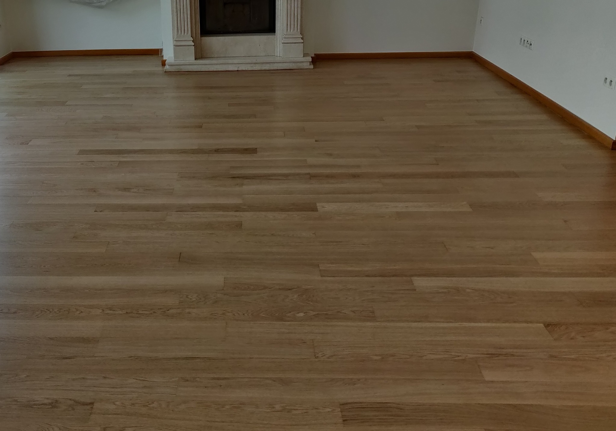 Wypolerowana, jasna podłoga parkietowa w Bydgoszczy po renowacji, widoczny fragment kominka z marmurową obudową i listwy przypodłogowe.