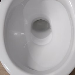 Usługi Sprzątające Joanna - Biała, ceramiczna muszla klozetowa marki Cersanit, widok z góry, po dokładnym umyciu, z widocznymi płytkami podłogowymi imitującymi drewno.