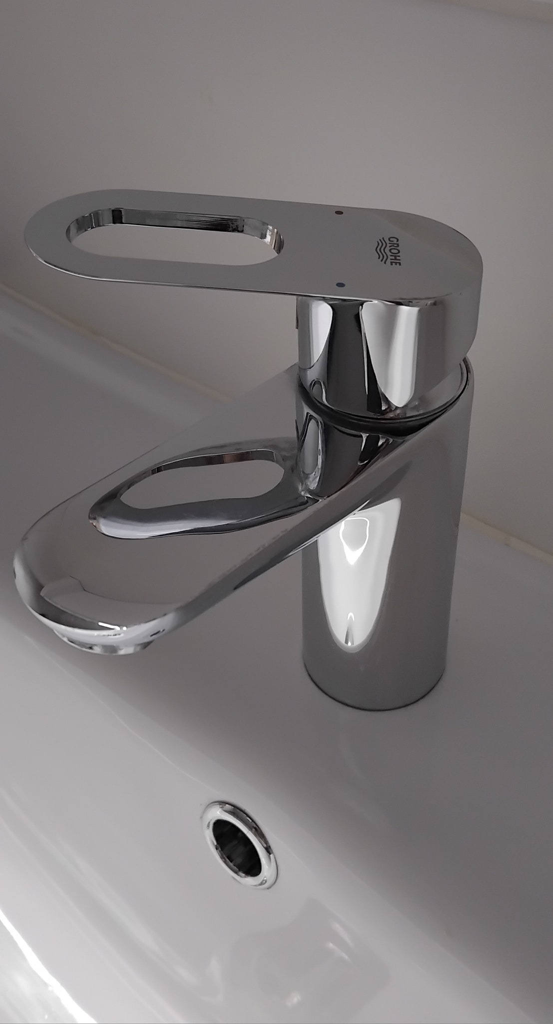 Błyszcząca, chromowana bateria Grohe zamontowana na białej umywalce, widok z góry.