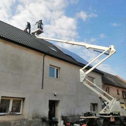 WITEK Łukasz Witkowski - Montaż paneli słonecznych na dachu domu w Ziębicach z użyciem podnośnika koszowego; dwóch pracowników w koszu na tle błękitnego nieba.