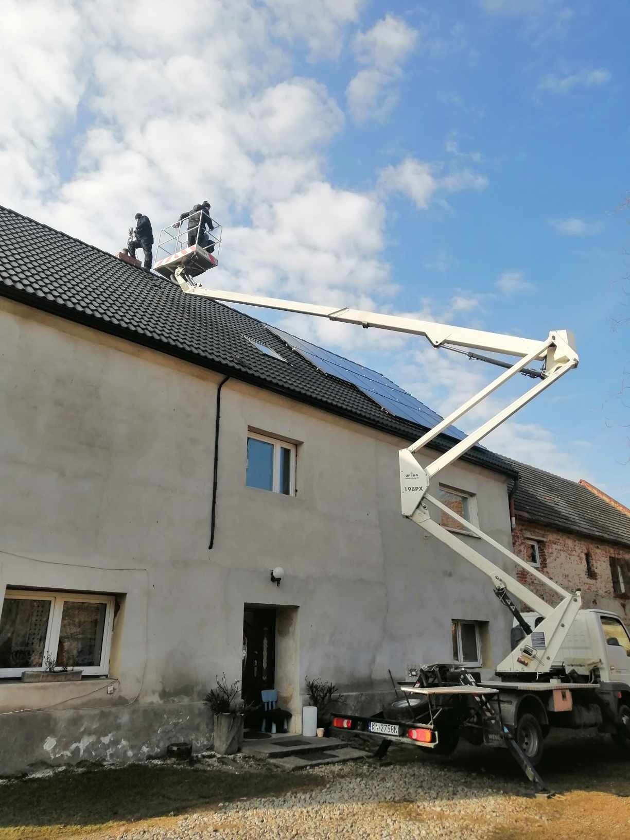 Montaż paneli słonecznych na dachu domu w Ziębicach z użyciem podnośnika koszowego; dwóch pracowników w koszu na tle błękitnego nieba.