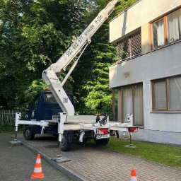 EHC Karol Zagajewski sp. k. - Podnośnik koszowy Ruthmann H-22m ustawiony na chodniku z rozłożonymi podporami, z widocznym numerem telefonu i tablicą rejestracyjną K4 EHC, obok budynku z oknami i balkonem