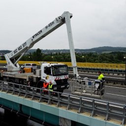 EHC Karol Zagajewski sp. k. - Pracownicy w odblaskowych kamizelkach obsługują podnośnik koszowy H-45m z platformą na moście, widoczny numer telefonu kontaktowego i logo firmy EHC Karol Zagajewski.