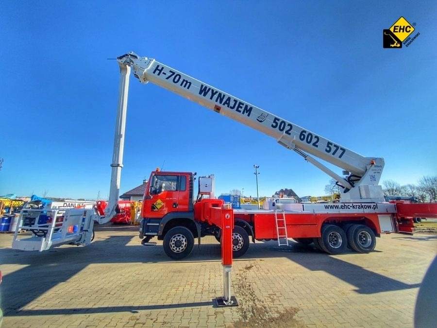 Czerwony podnośnik koszowy H-70m z wysuniętym ramieniem i koszem, zaparkowany na placu, na ramieniu widoczny numer telefonu do wynajmu, logo firmy EHC w prawym górnym rogu.