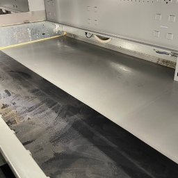 V&J GROUP SPÓŁKA Z OGRANICZONĄ ODPOWIEDZIALNOŚCIĄ - Wnętrze przemysłowej zmywarki do naczyń, połowa podłogi umyta, połowa brudna, widoczne metalowe ściany i otwory wentylacyjne.