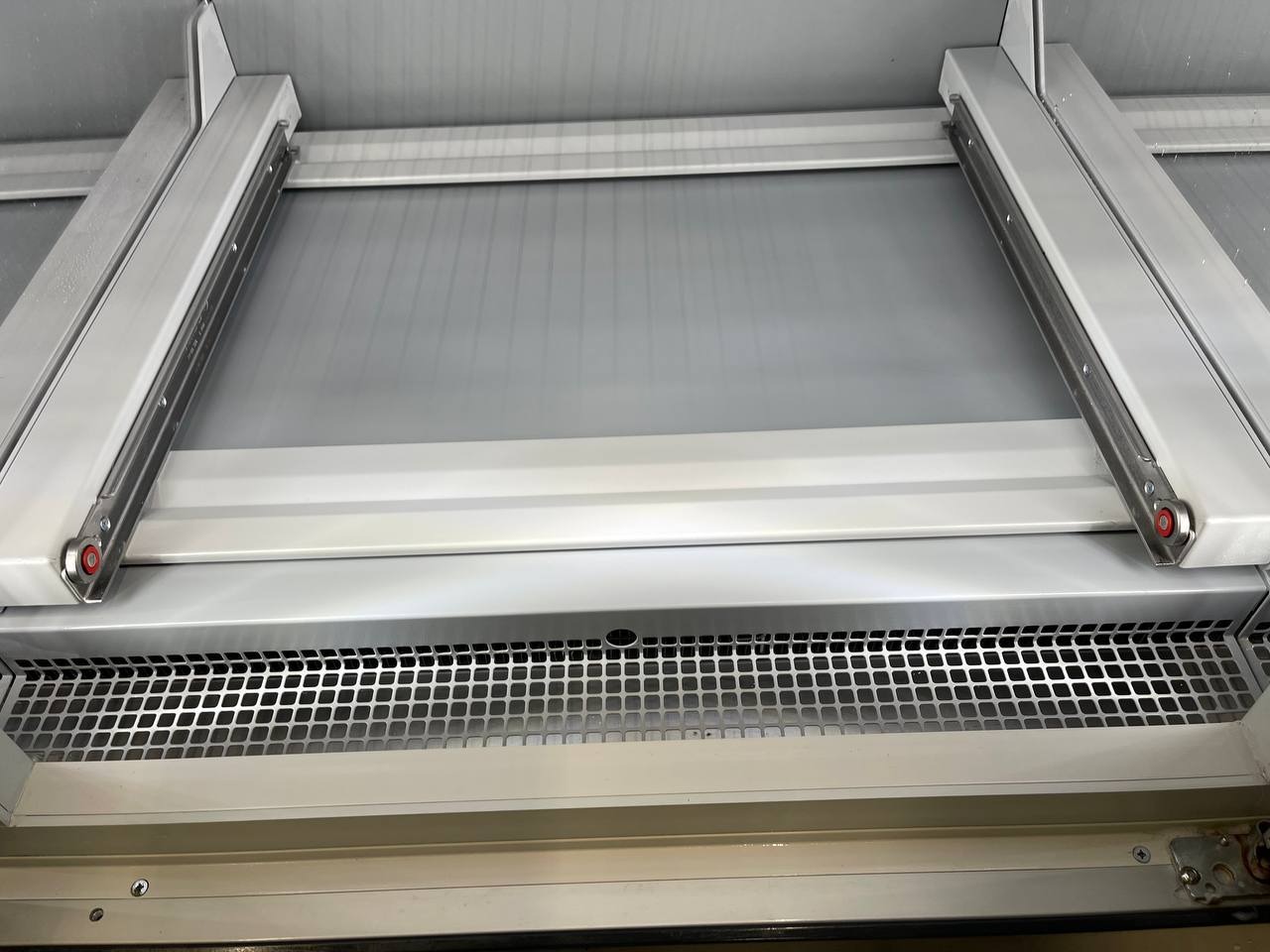 Szczegółowe ujęcie ramy okiennej z metalowymi prowadnicami i kratką wentylacyjną, widoczne ślady użytkowania i drobne zabrudzenia.