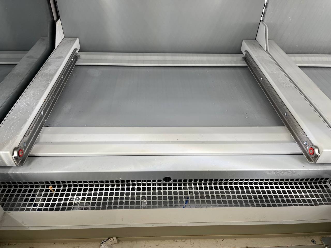 Wnętrze piekarnika przemysłowego z widocznymi prowadnicami i kratką wentylacyjną, osadzony brud i plamy na metalowych powierzchniach.