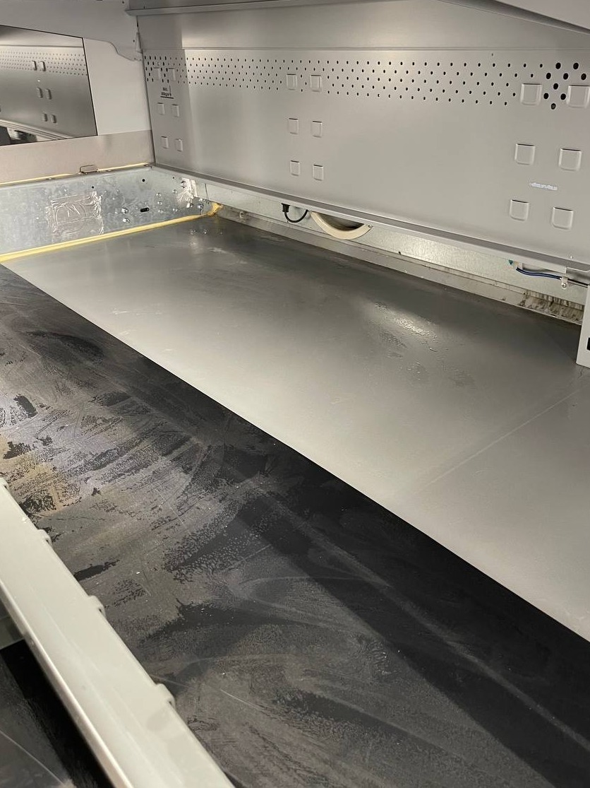 Wnętrze przemysłowej zmywarki do naczyń, połowa podłogi umyta, połowa brudna, widoczne metalowe ściany i otwory wentylacyjne.