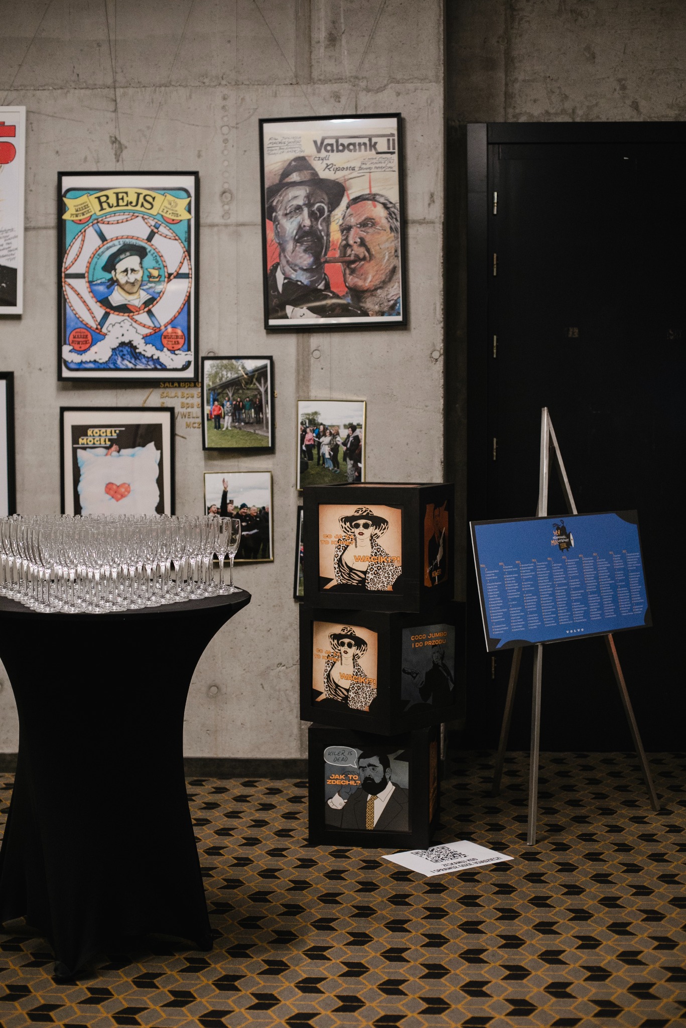 Dekoracje imprezowe: kieliszki na stole, plakaty filmowe (Vabank, Rejs), czarne kostki z motywami filmowymi i tablica z listą gości na sztaludze.