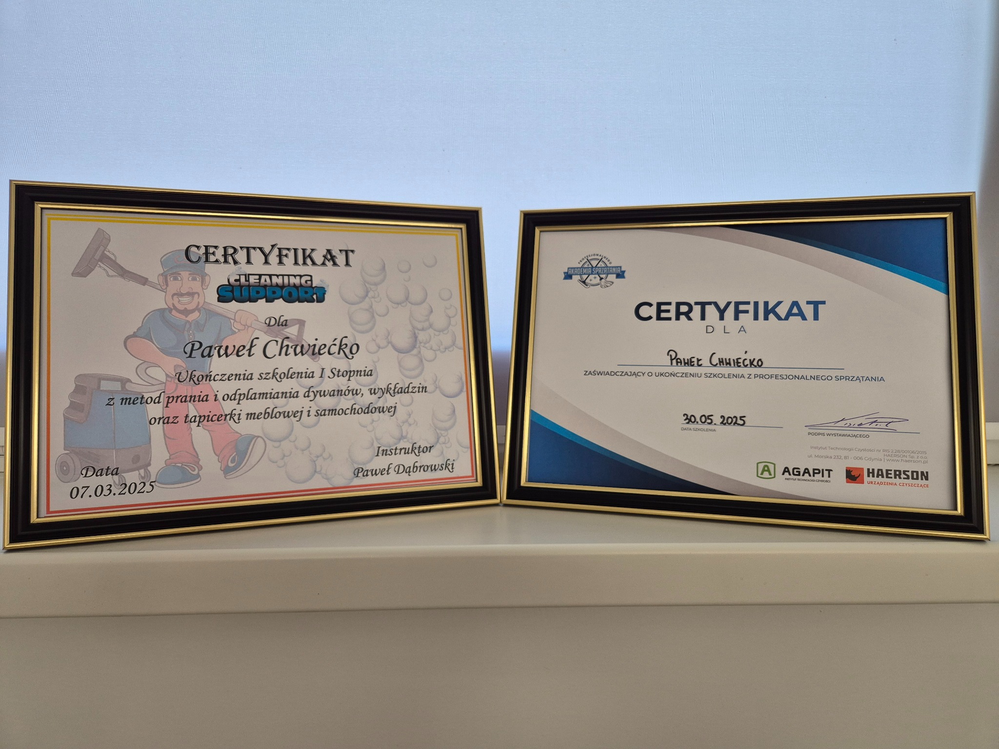 Dwa oprawione certyfikaty ukończenia szkoleń z zakresu prania dywanów i tapicerki meblowej, z datami 07.03.2025 i 30.05.2025, umieszczone obok siebie.