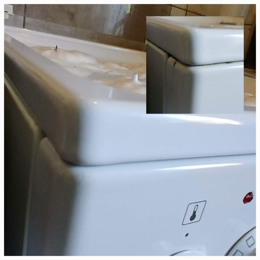 Czyszczenie kuchenki gazowej: biała emaliowana powierzchnia z pianą i brudem w rogu, zbliżenie na detale zabrudzeń przed czyszczeniem.